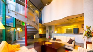 A modern hotel lobby with a central seating area, a staircase, and a reception desk.