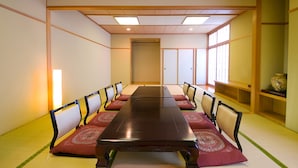 A traditional Japanese-style meeting room with tatami flooring, a long wooden table, and low wooden walls.