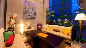 A modern living room with a sofa, armchairs, a coffee table, and a large window offering a city view.
