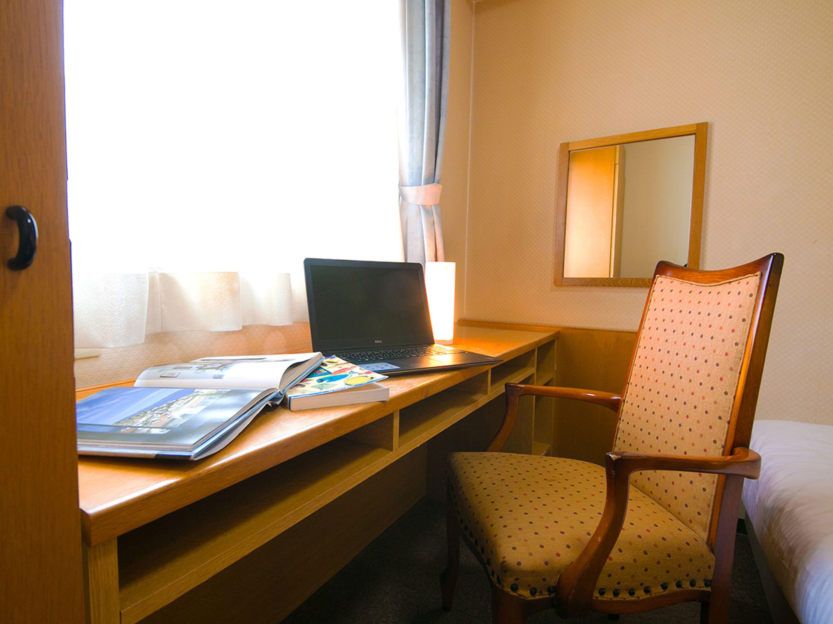 A hotel room with a wooden desk, a laptop, a chair, and a bed.
