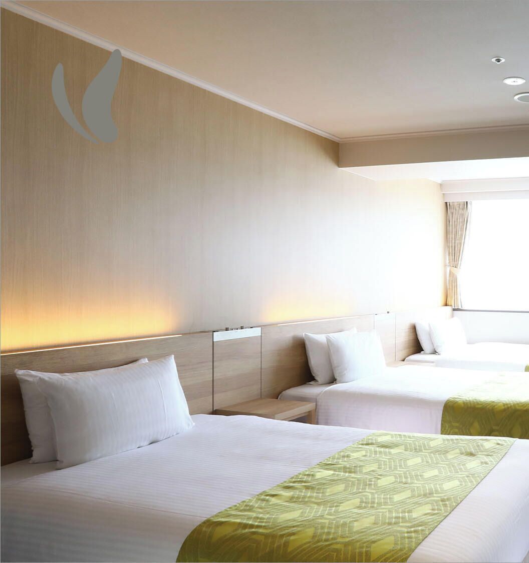 A hotel room with two beds, a headboard, a bedside table, and a window with curtains.