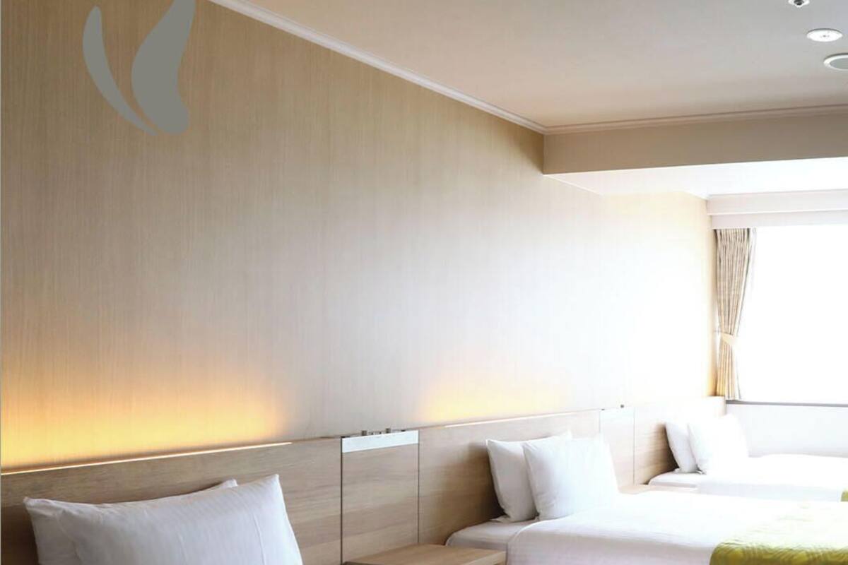 Habitación de hotel con dos camas, cabecero, mesita de noche y ventana con cortinas.