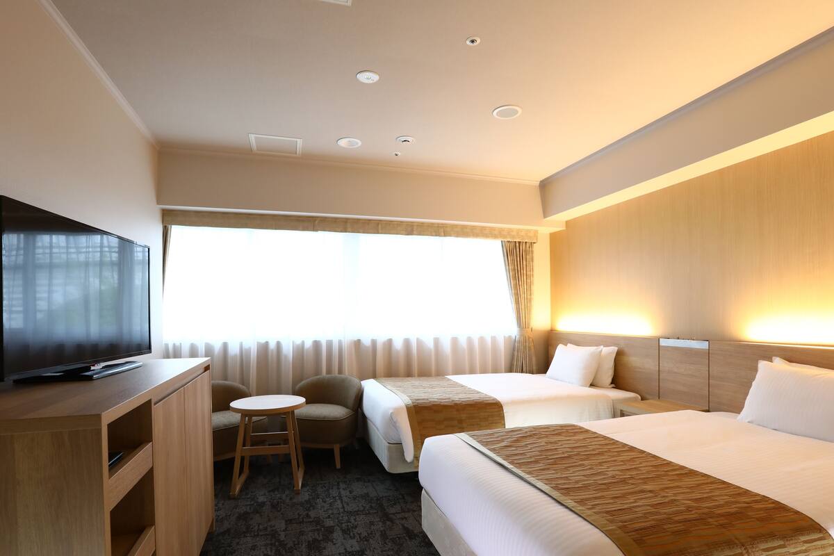 Una habitación de hotel con televisor de pantalla plana, dos camas, una mesita y una silla.