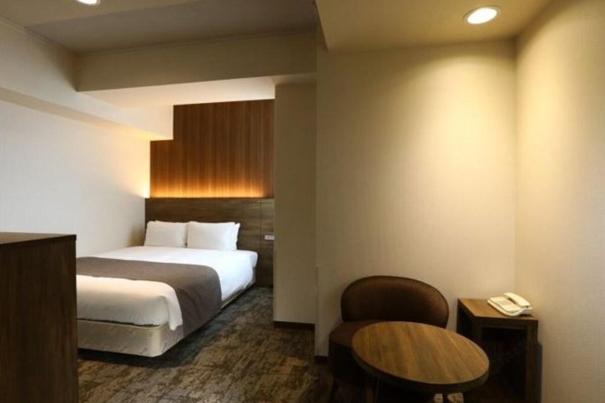 Una habitación de hotel con una cama, cabecera de madera, una mesita redonda y un teléfono.