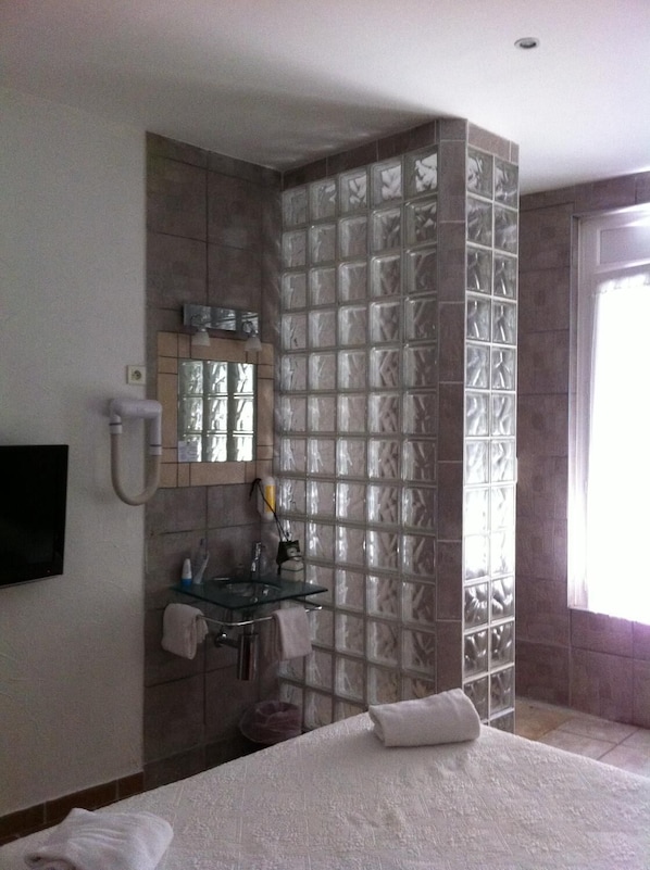 Baño de hotel con separador de bloques de vidrio, un lavamanos con espejo y una toalla en el suelo.