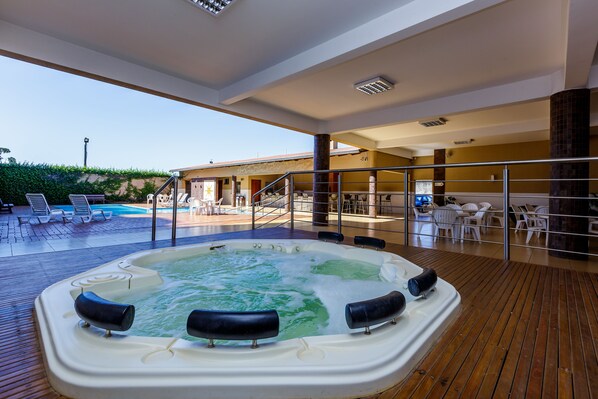 A hot tub on a wooden deck with a pool and lounge chairs in the background. -  Luz Hotel by Castelo Itaipava (Foz do Iguaçu)