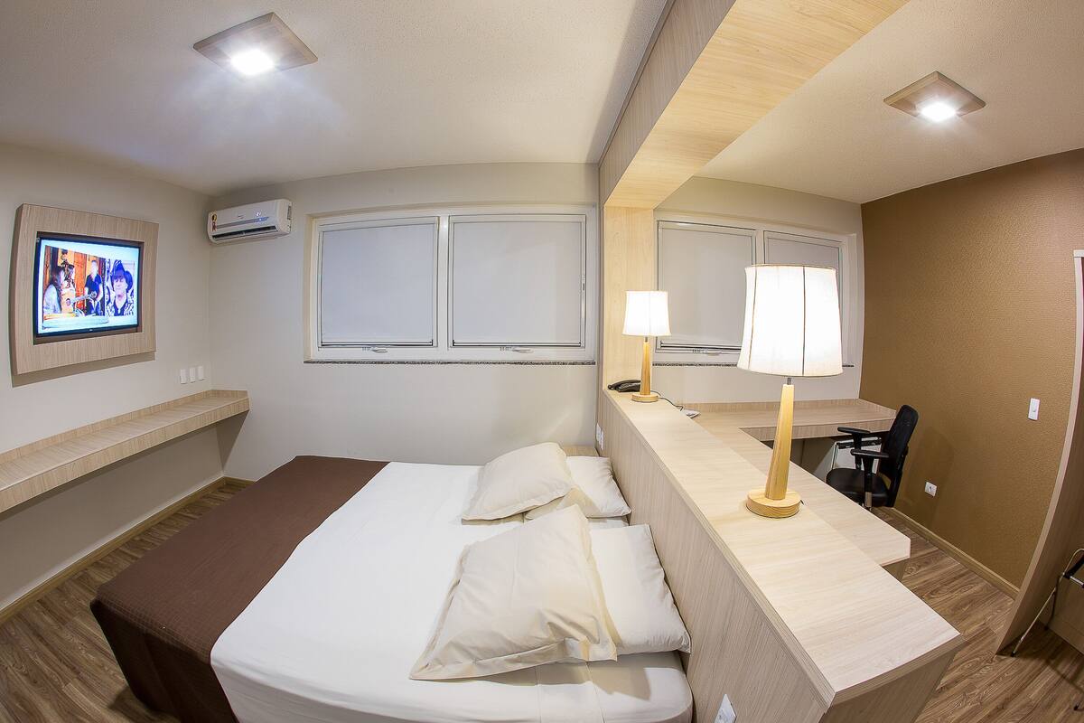 Habitación de hotel con cama, escritorio, silla, televisión y aire acondicionado.