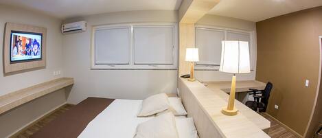 A hotel room with a bed, a desk, a chair, a TV, and an air conditioning unit.