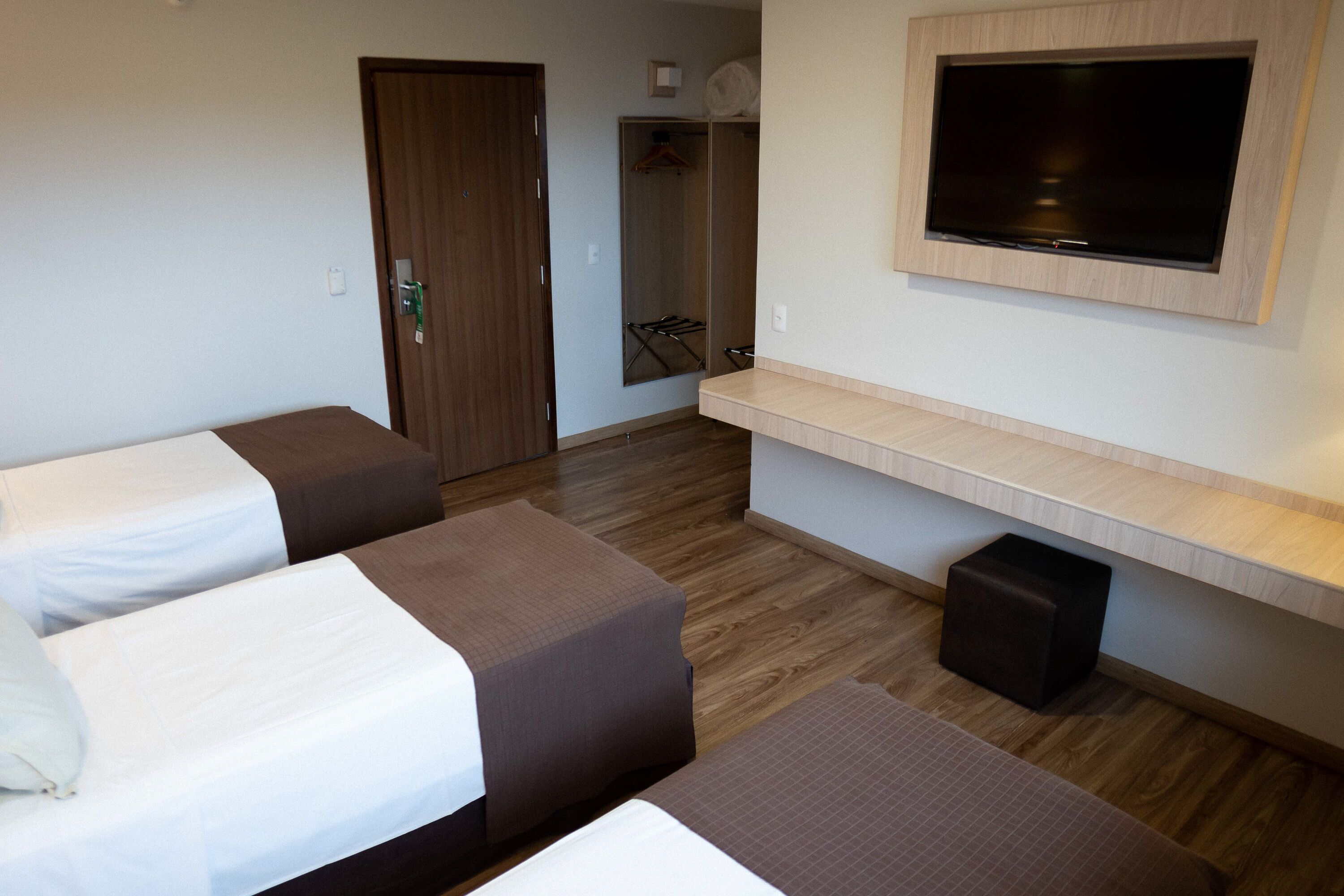 Habitación de hotel con dos camas, un televisor montado en la pared y suelo de madera.