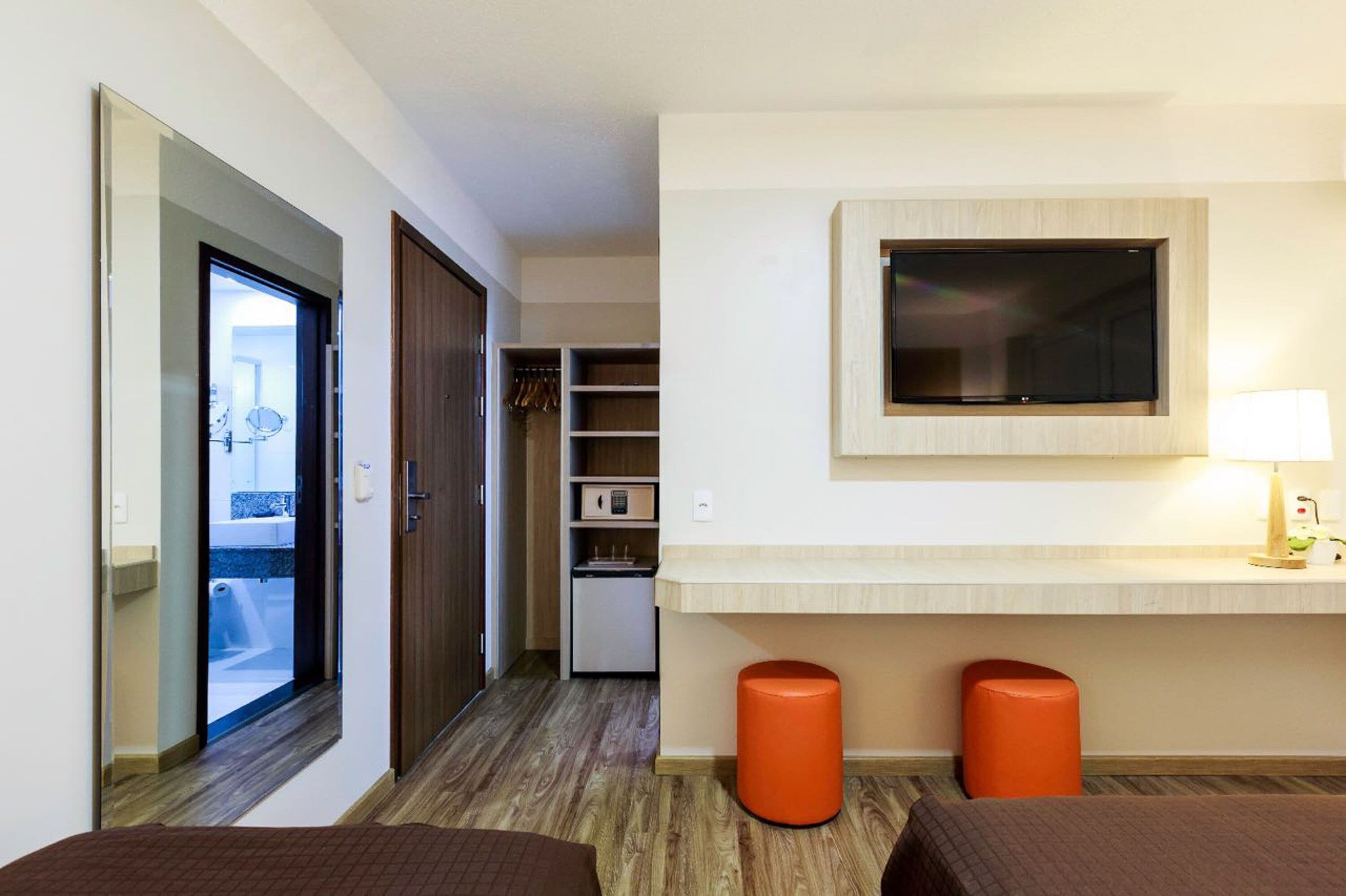 Ein Hotelzimmer mit einem Bett, einem an der Wand montierten Fernseher, einer kleinen Küchenzeile und einem Badezimmer, dessen Dusche und Toilette durch eine geöffnete Tür sichtbar sind.