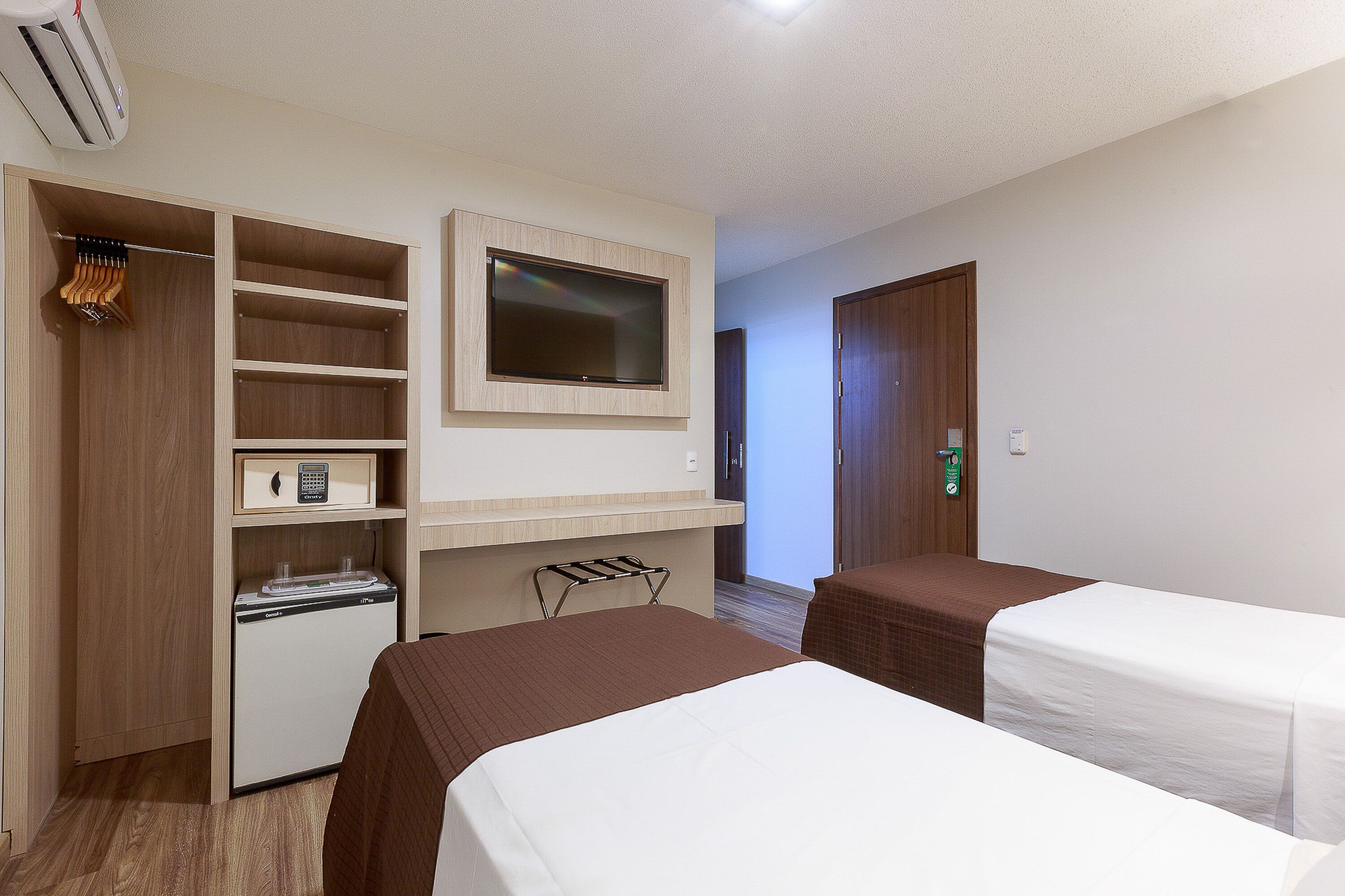 Ein Hotelzimmer mit zwei Betten, einem Fernseher, einer Minibar, einem Schreibtisch und einem Kleiderschrank.