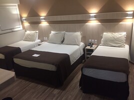 Ein Hotelzimmer mit drei Betten, einem Schreibtisch und einem Telefon auf dem Nachttisch.