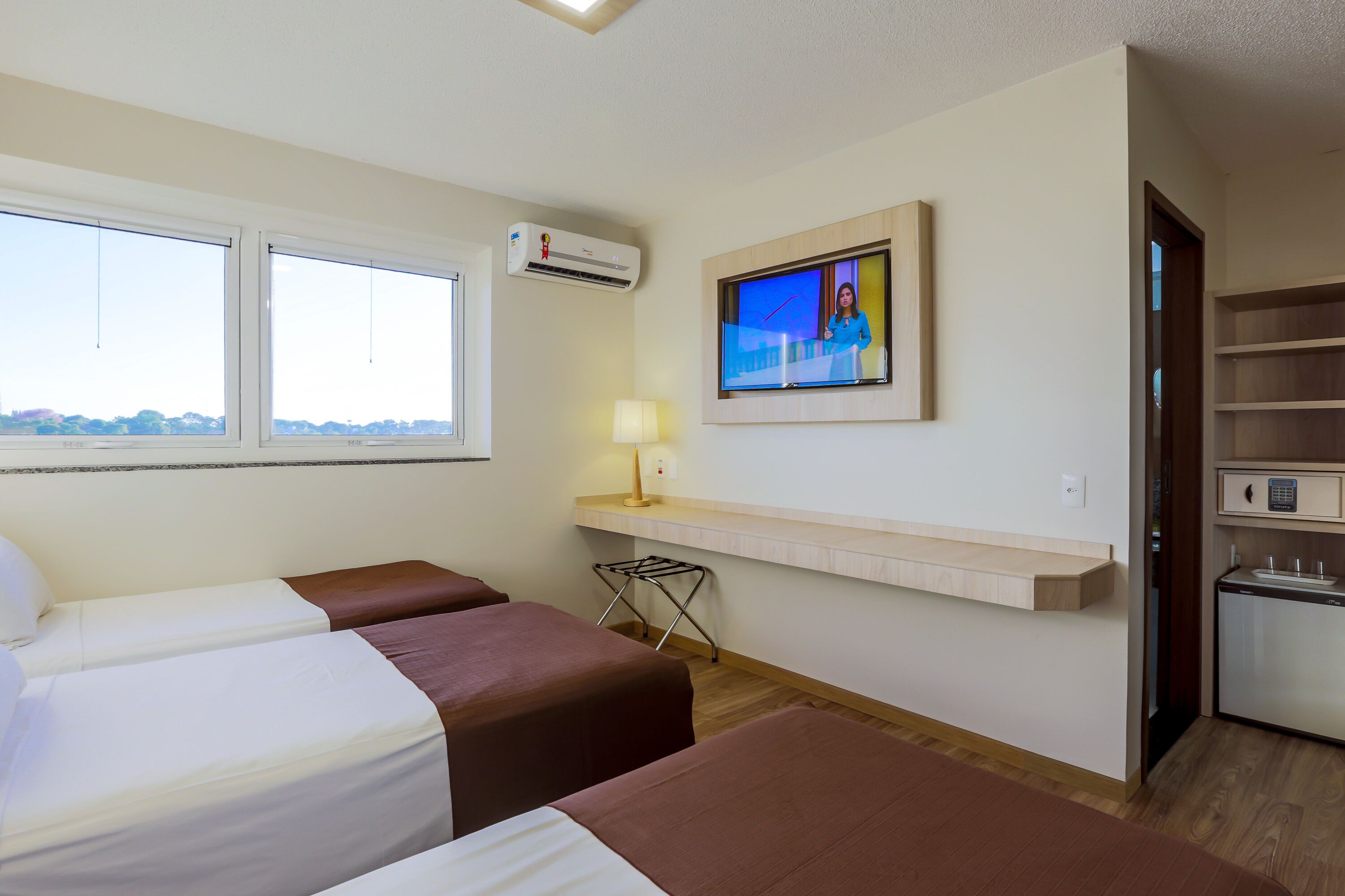 Habitación de hotel con dos camas, un televisor, un escritorio pequeño con lámpara y una kitchenette.