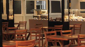 Un comedor con mesas y sillas de madera, mostrador tipo bufé e iluminación colgante.