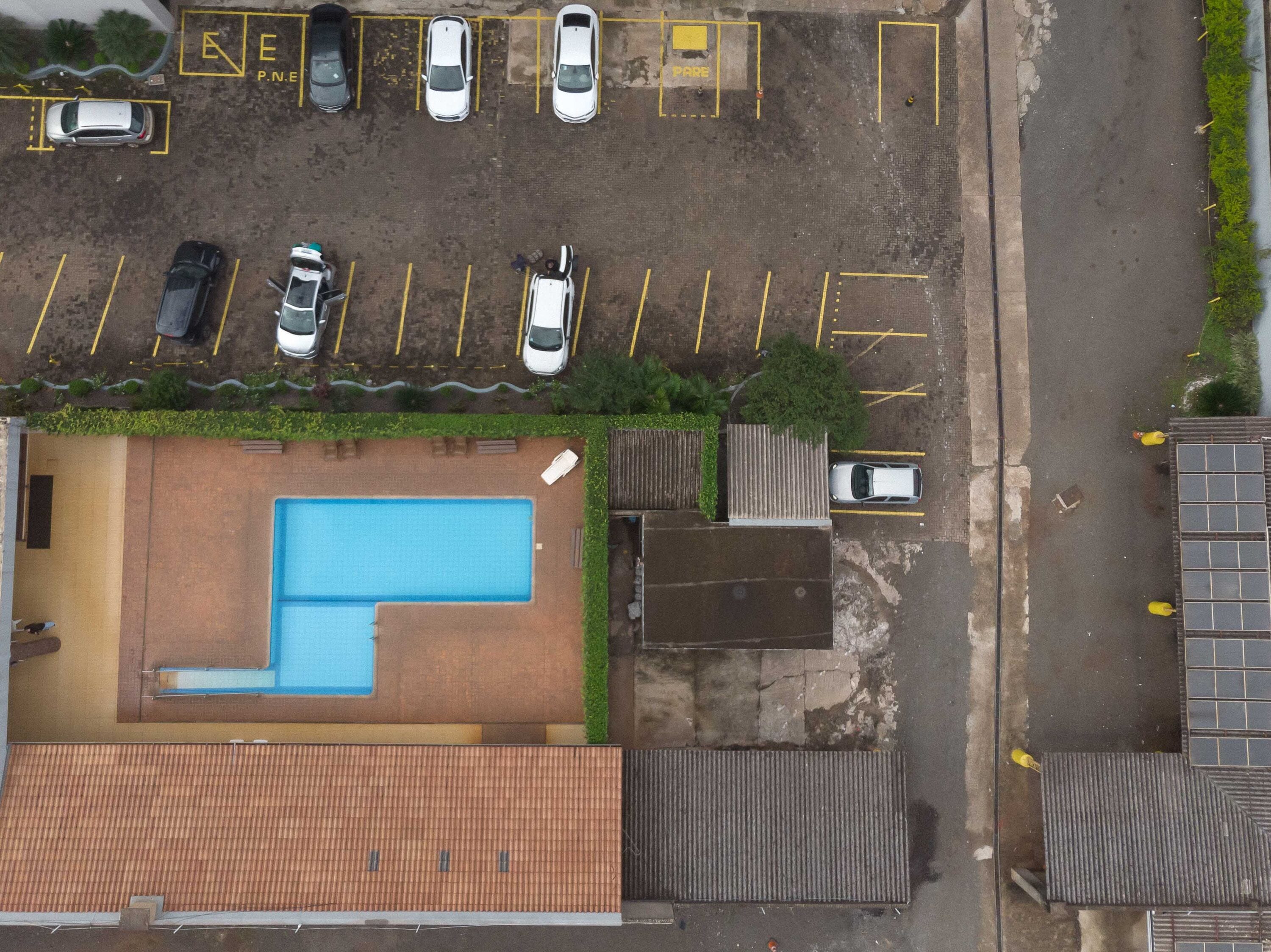 An aerial view of a parking lot with several cars, a swimming pool, and a building with a tiled roof.