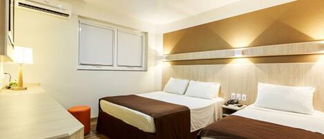 A hotel room with two beds, a desk, a lamp, an air conditioner, and a window.