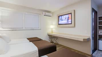 Habitación de hotel con dos camas, un televisor montado en la pared, una mesita con una lámpara y una estantería con un televisor.