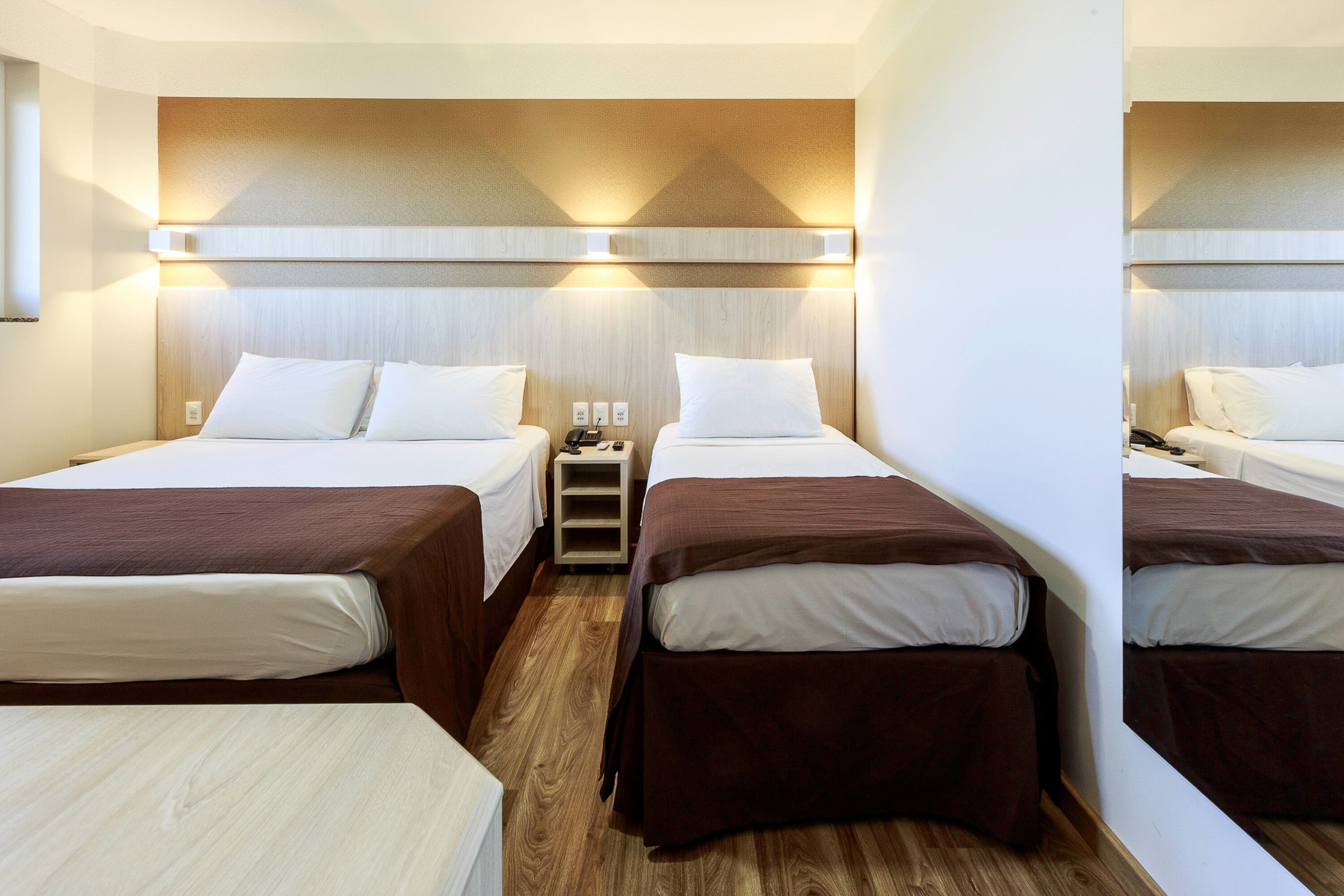 Habitación de hotel con dos camas, una mesita de noche y piso de madera.