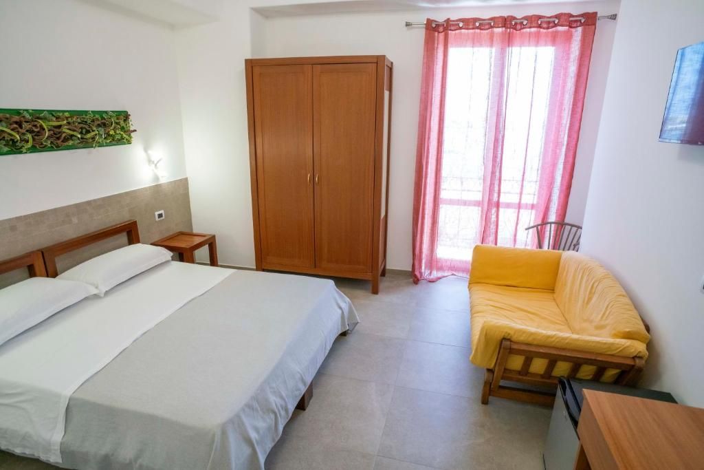 Un dormitorio con cama, armario, una mesita, sofá y ventana con cortinas.
