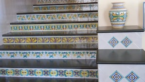 A staircase with colorful patterned tiles and a decorative vase on the landing.