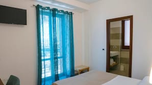A hotel room with a bed, a chair, a small table, a mirror, and a shower area.