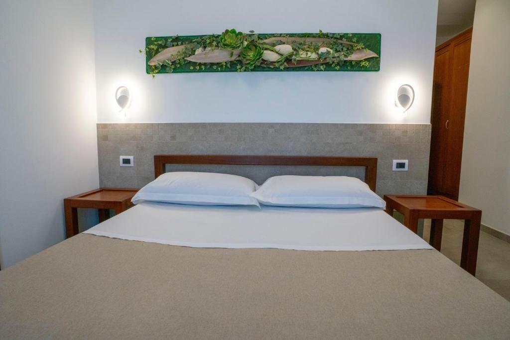 A neatly made bed with white linens and two pillows, flanked by two bedside tables with lamps, in a room with a grey headboard and a decorative wall piece above.