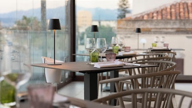 A restaurant with tables set for dining, a view of mountains, and a cityscape in the background.