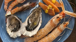 A plate of seafood including shrimp, lobster, and oysters, with a lemon wedge on a blue plate.