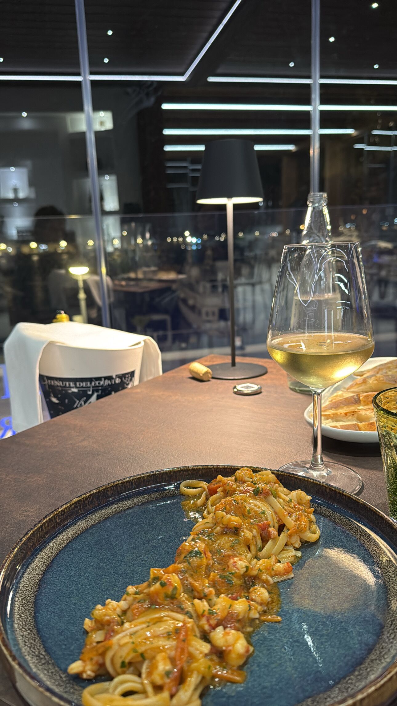 A dining table with a plate of pasta, a wine glass, and a bottle.