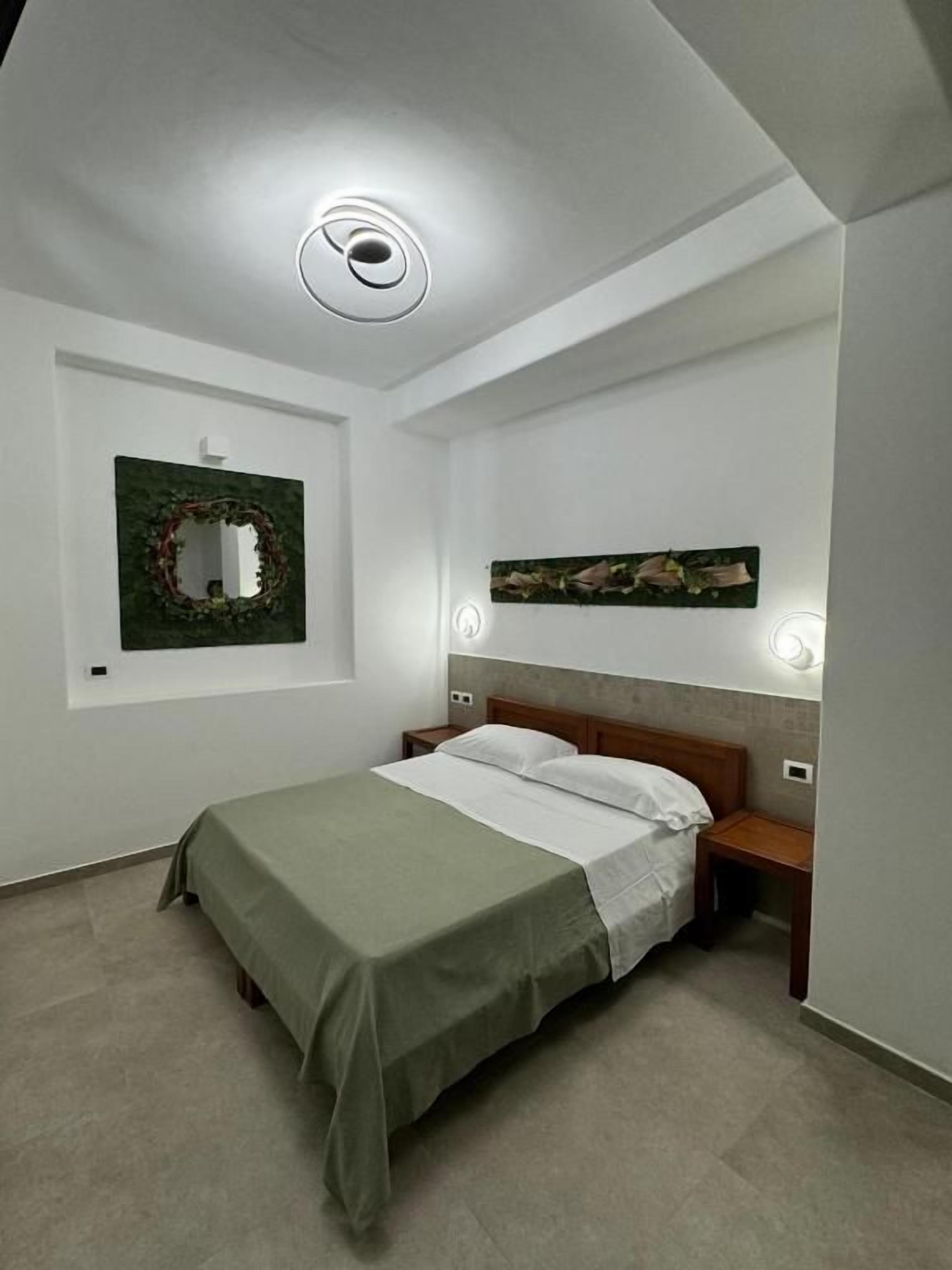 A bedroom with a bed, bedside tables, a wall-mounted light fixture, and a framed picture.