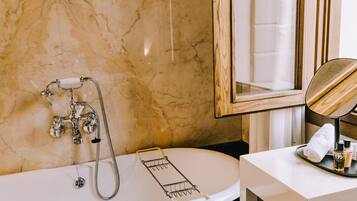 Ein Badezimmer mit Marmorwand, einer Badewanne inklusive Duschkopf, einem Handtuchhalter und einem Spiegel.