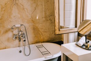 A bathroom with a marble wall, a bathtub with a shower head, a towel rack, and a mirror. - Maison Matilda (Treviso)