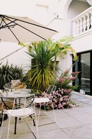 Un patio con mesa y sillas, rodeado de plantas y flores en macetas.