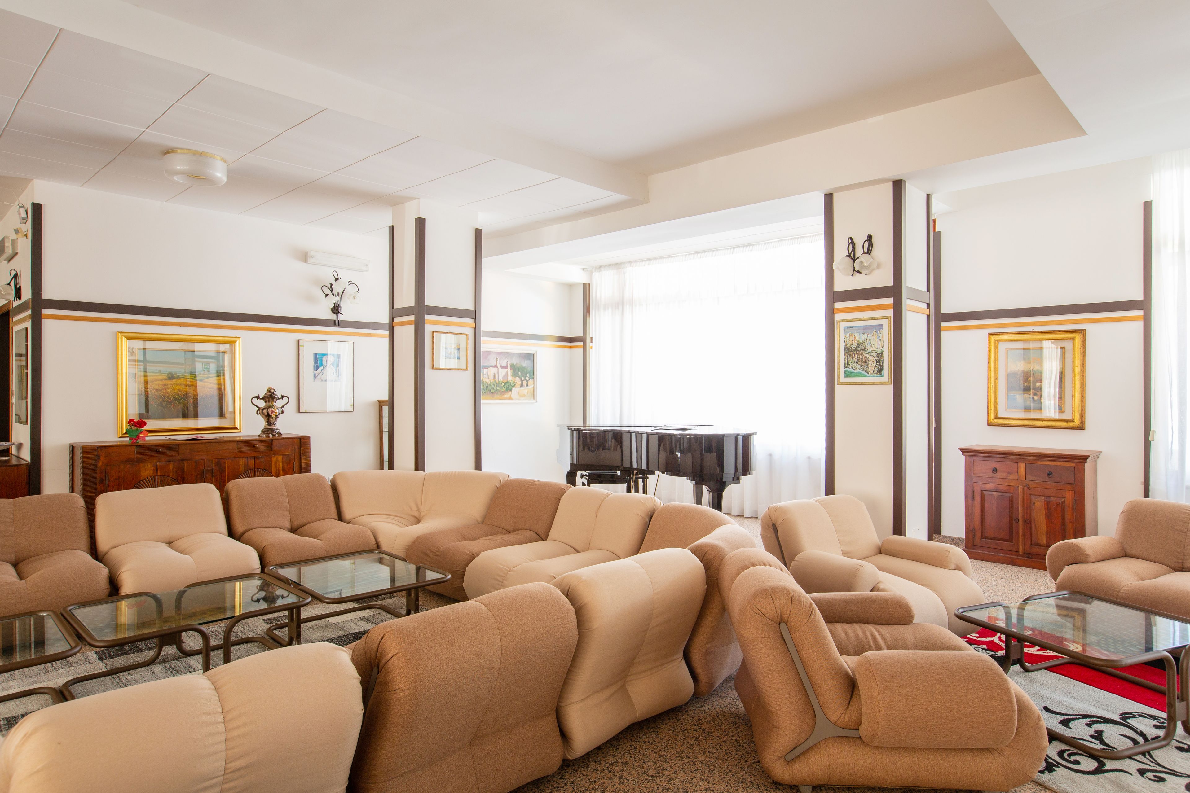 Un salón amplio con sofás color beige, una mesa de centro de vidrio y un piano de cola.