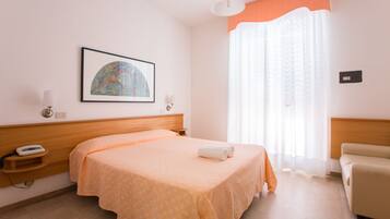 A hotel room with a bed, bedside table, lamp, and a painting on the wall.