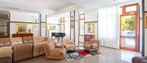A spacious living room with a sectional sofa, a glass coffee table, and a piano in the background.
