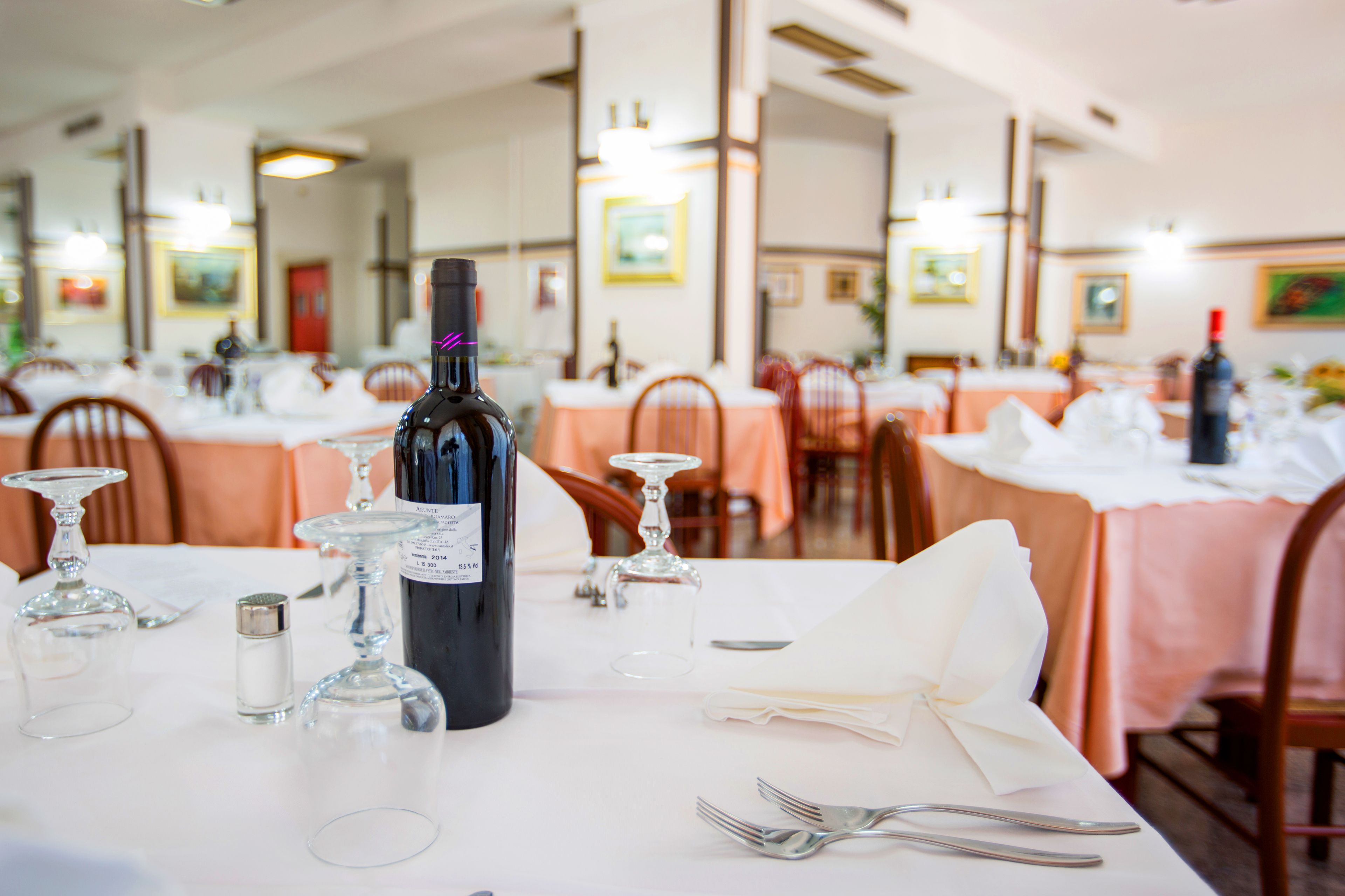 A restaurant setting with tables set for dining, featuring wine bottles and glasses.