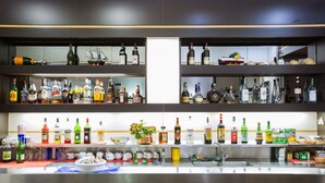 Uma área de bar com prateleiras cheias de garrafas de bebidas, copos e utensílios de bar.