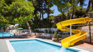 Piscina com escorregador amarelo, cadeiras de descanso e vista para árvores.