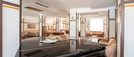 A grand piano in a spacious living area with a modern design, including a large mirror reflecting the room.