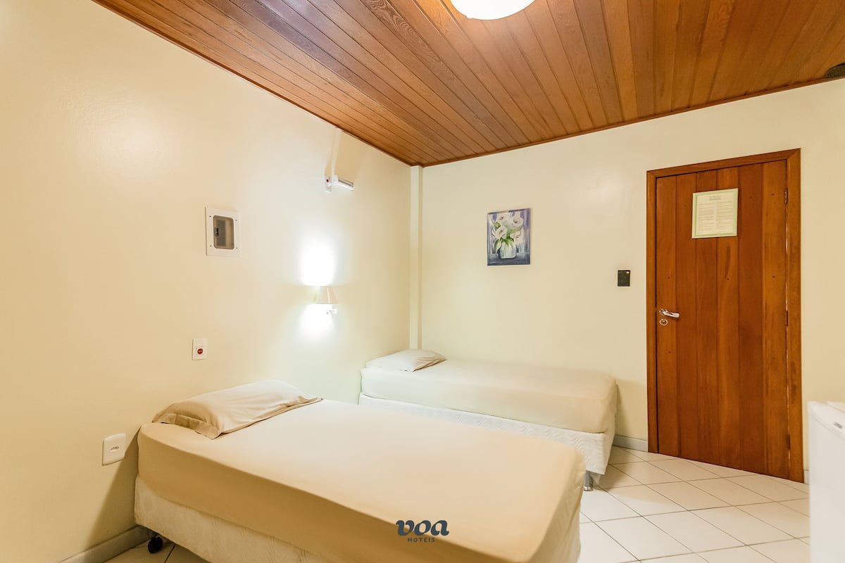 A hotel room with two beds, a wooden ceiling, a door, and a small painting on the wall.