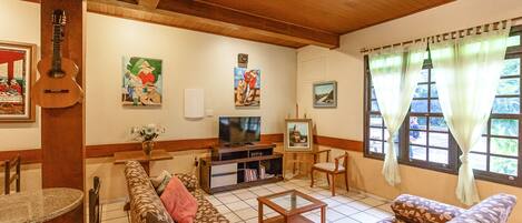 Een woonkamer met een houten plafond, een televisie, een gitaar en diverse kunstwerken aan de muren.