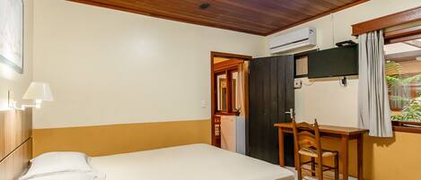 Habitación de hotel con cama, escritorio, silla, equipo de aire acondicionado y ventana con cortinas.