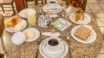 Una mesa redonda con alimentos para el desayuno, como tostadas, mantequilla, mermelada, una tetera y una taza de café.