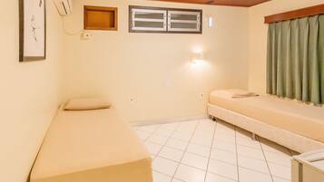 A small, single-room hotel room with a bed, a bench, a window, and a wall-mounted air conditioner.