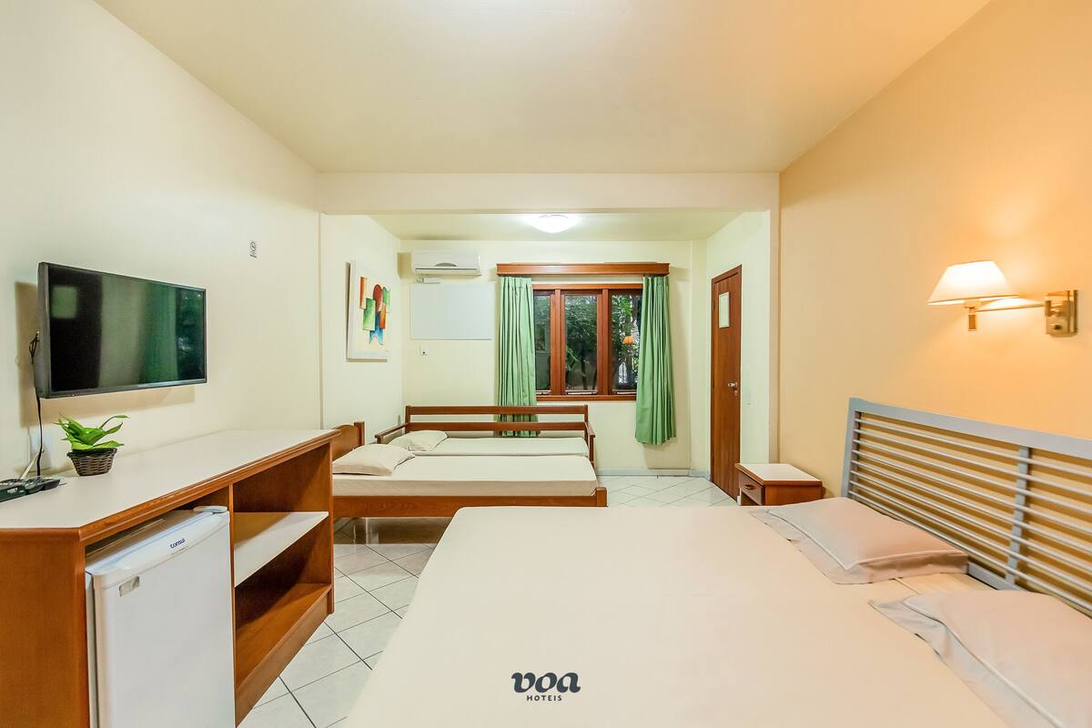 A hotel room with a bed, a desk with a TV, a mini-fridge, and a window with curtains.