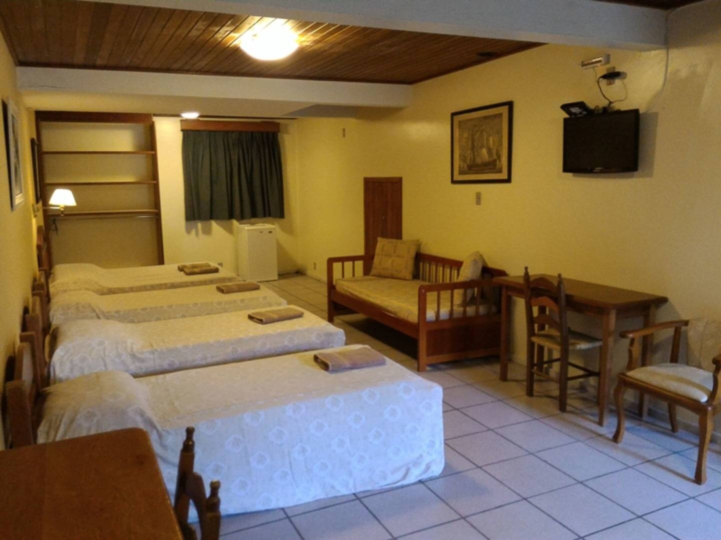 Una habitación con dos camas, un escritorio, una silla, una mesita, un televisor y una ventana con cortinas.