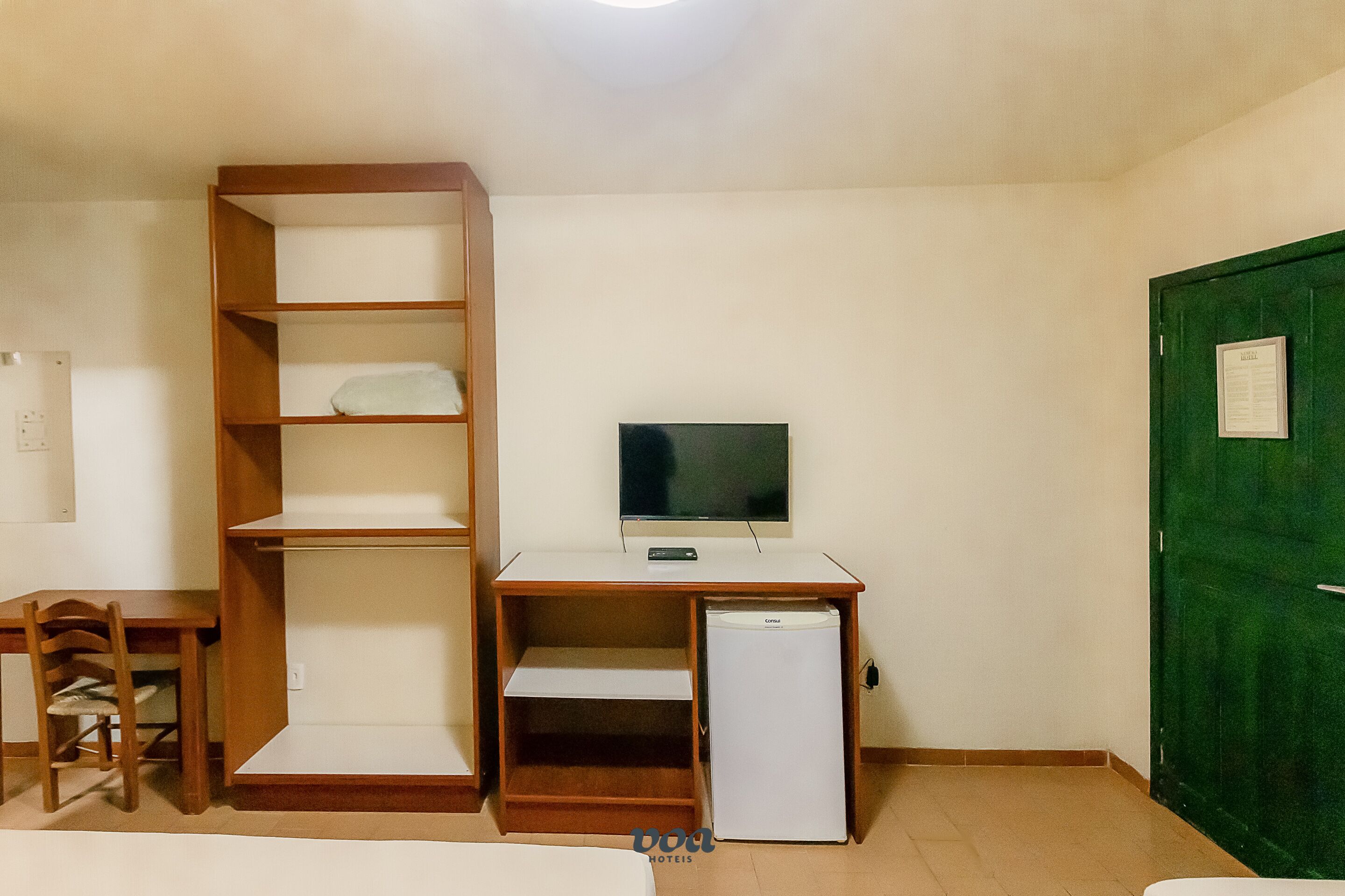 A room with a wooden desk, a television, and a small refrigerator.