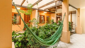 A hammock in a sunlit indoor space with wooden beams and tiled floors, surrounded by various plants. - VOA Samuka Hotel (Florianópolis)