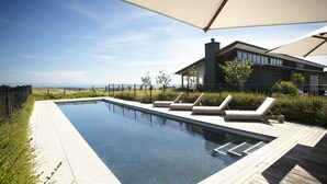 Une piscine extérieure moderne, dotée de chaises longues, d’une terrasse en bois et offrant une vue sur l’océan.